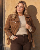 Milla i brun mockajacka från Missy, sandfärgad tröja från Haust och bruna jeans från Frank Lyman mot en solig vägg